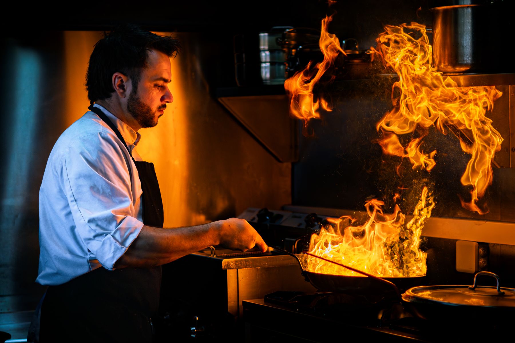 Chef working a pan of open flame in a dark professional kitchen